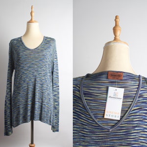 Può includere: Un top a maniche lunghe con scollo a V con un motivo a righe blu, gialle e bianche. Il top è esposto su un manichino. Un'etichetta recita "Missoni" e "thenewnew VINTAGE STORE".