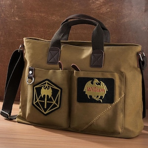 May include: A tan canvas messenger bag with two top handles and a shoulder strap. The front features two pockets, one with a black hexagonal patch displaying a gold axe, and the other with a black rectangular patch showing a gold dragon and the name William.