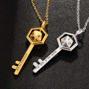 May include: Two gold and silver key necklaces with a dice charm. The gold necklace has the inscription "Roll for Adventure" and the silver necklace has the inscription "The dice is my guide".