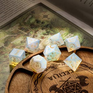 May include: Set of seven iridescent blue and gold dice with celestial and astrological symbols on a wooden tray with the word "CECILIA" engraved on it.