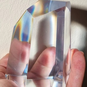 May include: A clear glass prism with iridescent rainbow colors reflecting on the surface. The prism is shaped like a rectangular block with beveled edges.