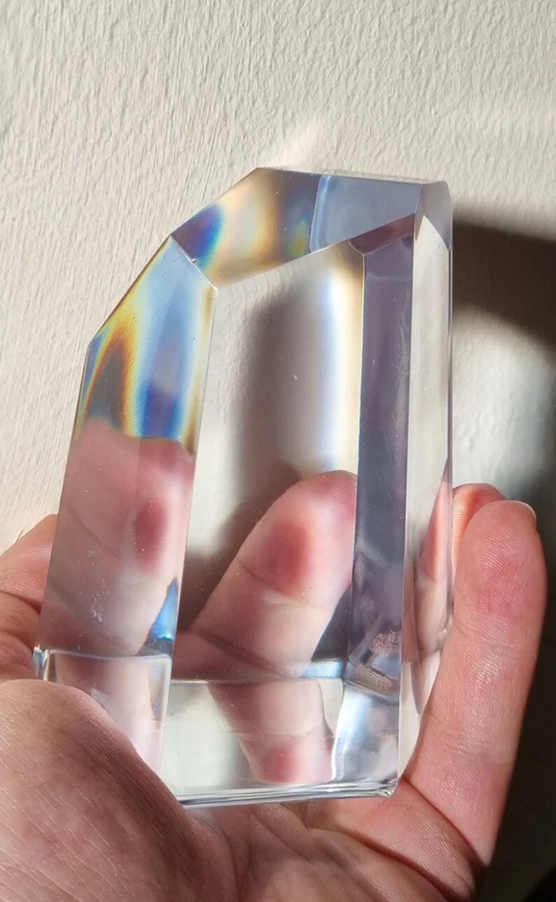 May include: A clear glass prism with iridescent rainbow colors reflecting on the surface. The prism is shaped like a rectangular block with beveled edges.