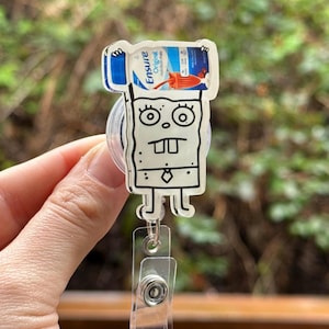 May include: A cartoon character resembling SpongeBob SquarePants holding a bottle of Ensure Original Nutrition Shake. The character is attached to a clear plastic retractable badge holder.