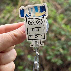 May include: A white cartoon character with a black outline holding a bottle of Ensure Original Nutrition Shake. The character is wearing a tie and has a surprised expression. The character is attached to a clear plastic retractable badge holder.