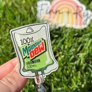 May include: A clear plastic badge holder shaped like an IV bag with a green Mountain Dew logo and the text "100% Mountain Dew" and "500 ML".