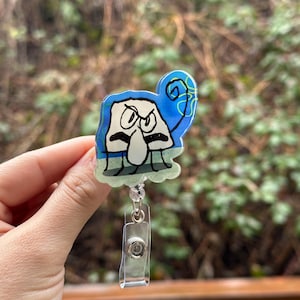 May include: A blue and white cartoon character with a grumpy expression is featured on a clear plastic badge holder. The character has a large nose and is wearing a blue hat with a green swirl. The badge holder has a clear plastic clip.
