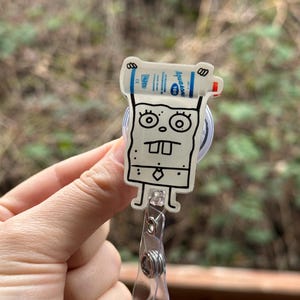 Puede incluir: Un personaje de dibujos animados blanco con contorno negro sosteniendo una botella azul y blanca de desinfectante de manos. El personaje lleva corbata y tiene una gran sonrisa. El personaje est&aacute; unido a un portagajes retr&aacute;ctil de pl&aacute;stico transparente.