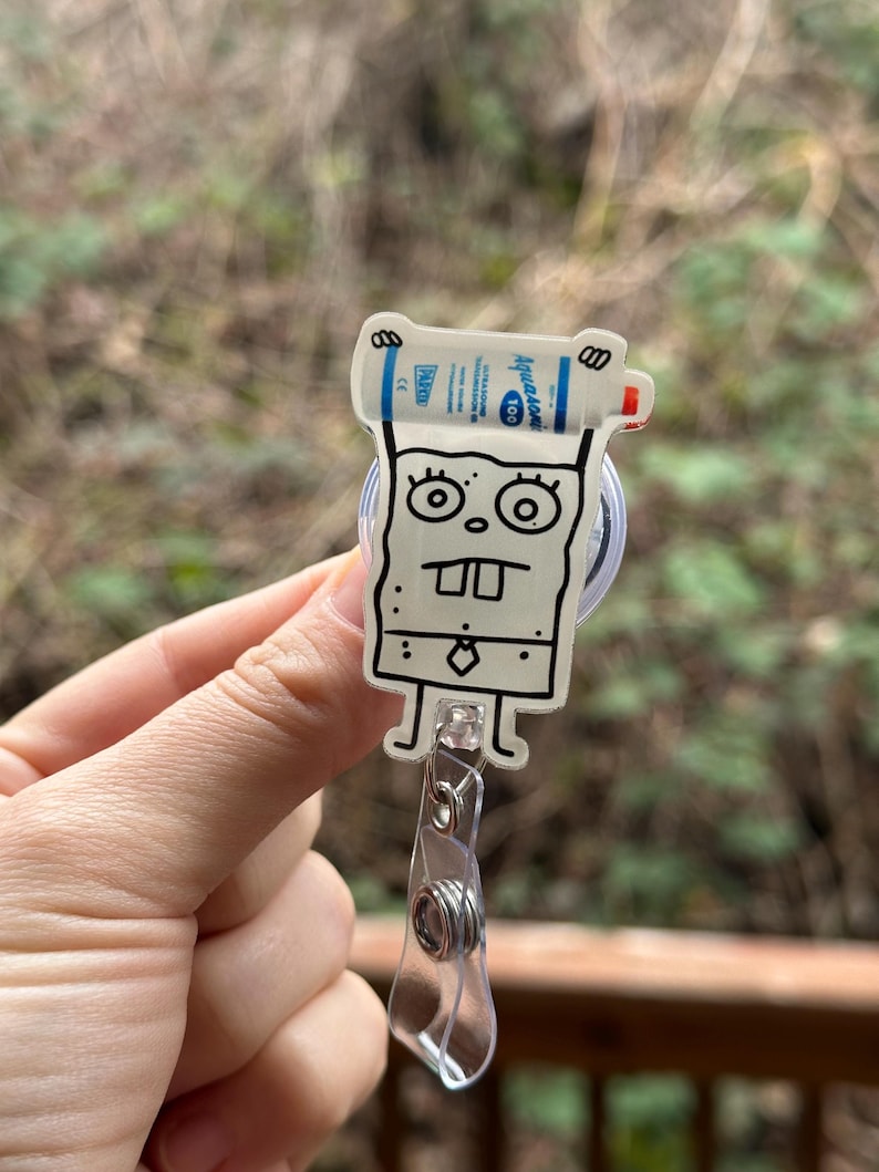 Puede incluir: Un personaje de dibujos animados blanco con contorno negro sosteniendo una botella azul y blanca de desinfectante de manos. El personaje lleva corbata y tiene una gran sonrisa. El personaje est&aacute; unido a un portagajes retr&aacute;ctil de pl&aacute;stico transparente.