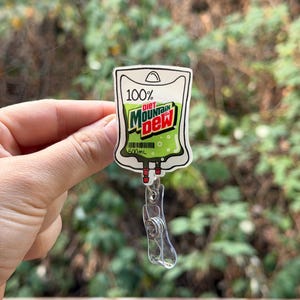 May include: A Diet Mountain Dew badge reel with a clear plastic clip. The badge reel features a white and green design resembling a beverage bag, with the words "Diet Mountain Dew" and "500mL" printed on it.
