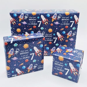 May include: Three blue gift boxes with a space-themed design. The boxes are decorated with rockets, planets, stars, and astronauts. The text on the boxes reads "Hope your birthday is out of this world" and features the number "7".