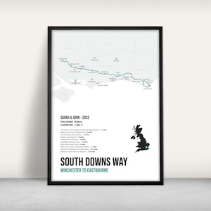 May include: A black and white map of the South Downs Way, a 100-mile hiking trail in England, with a teal line tracing the route from Winchester to Eastbourne. The map includes a smaller map of the United Kingdom with the trail location highlighted. The text "SARAH & JOHN - 2022" is at the top of the map, along with the total distance and elevation gain.