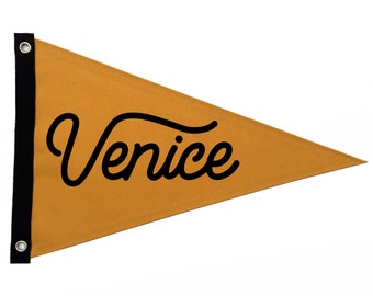 May include: Mustard yellow pennant flag with the word "Venice" in black script. The flag has a black border on the left side with two silver grommets. The pennant is triangular in shape.