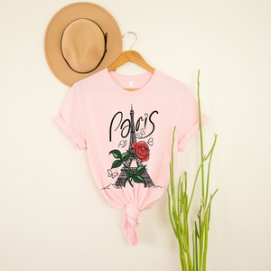 May include: Pink t-shirt with a graphic of the Eiffel Tower and a red rose with the word "Paris" written in cursive.