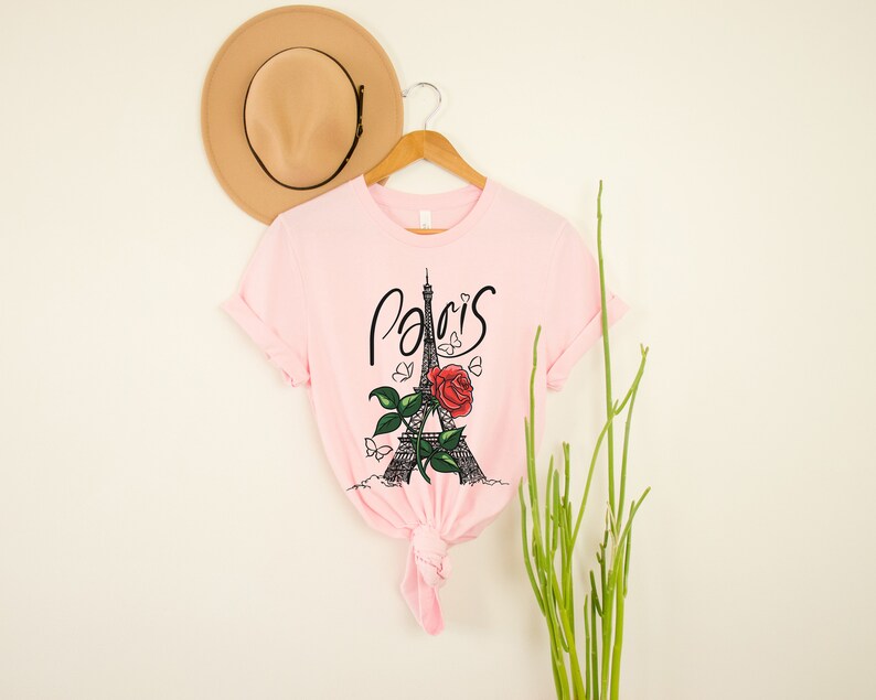 May include: Pink t-shirt with a graphic of the Eiffel Tower and a red rose with the word "Paris" written in cursive.