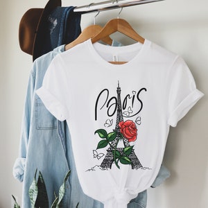 May include: White t-shirt with a black and white illustration of the Eiffel Tower with a red rose and butterflies. The text "Paris" is written in black cursive above the tower.