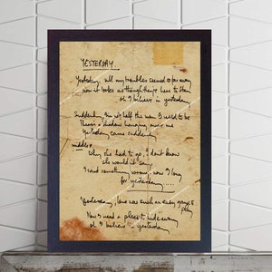 Puede incluir: Una impresión enmarcada de letras escritas a mano para la canción "Yesterday" de The Beatles. Las letras están escritas en un trozo de papel envejecido con un fondo marrón. Las letras están en tinta negra y están ligeramente descoloridas. El marco es negro y tiene un passe-partout blanco.