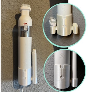 以下が含まれることがあります： 透明なゴミ箱と赤いボタンが付いた白いハンドヘルド掃除機。掃除機には取り外し可能な延長ワンドとブラシアタッチメントが付いています。掃除機は壁に取り付けられています。