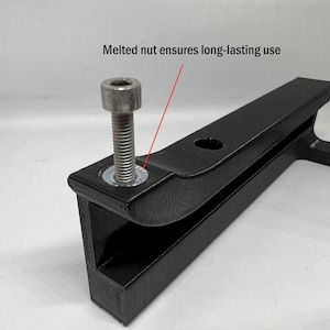 May include: A black 3D-printed bracket featuring a silver metal bolt and a washer. A red line points to the washer with the text "Melted nut ensures long-lasting use" printed above it. The bracket has a textured surface and a circular hole.