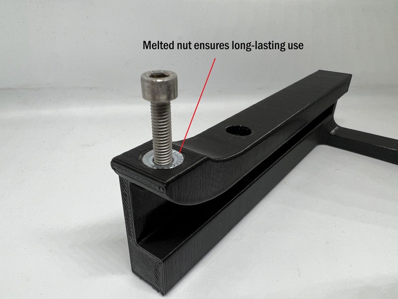 May include: A black 3D-printed bracket featuring a silver metal bolt and a washer. A red line points to the washer with the text "Melted nut ensures long-lasting use" printed above it. The bracket has a textured surface and a circular hole.