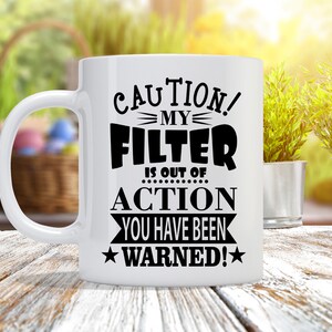 May include: White ceramic coffee mug with black text that reads "CAUTION! MY FILTER IS OUT OF ACTION YOU HAVE BEEN WARNED!" with stars on either side of the text.