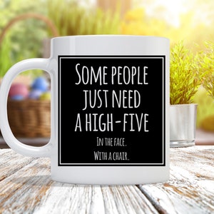 May include: White ceramic coffee mug with a black rectangle on the front. The rectangle has white text that reads "Some people just need a high-five. In the face. With a chair."