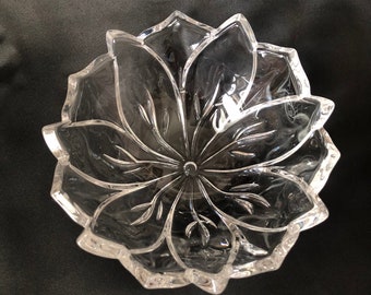 Puede incluir: Un cuenco de vidrio transparente con un diseño en forma de flor. El cuenco tiene un borde festoneado y está hecho de cristal.