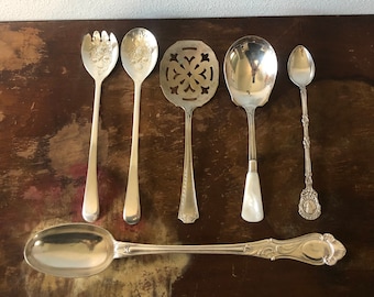 May include: Six silver spoons with ornate designs. The spoons are arranged in a row on a wooden surface.