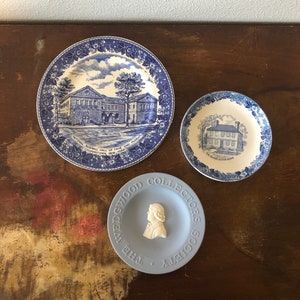 May include: Three blue and white ceramic plates with a blue and white floral design. The largest plate features a building with the text "National Baseball Hall of Fame and Museum Cooperstown, New York". The smallest plate features a portrait of a person with the text "The Wedgwood Collectors Society".