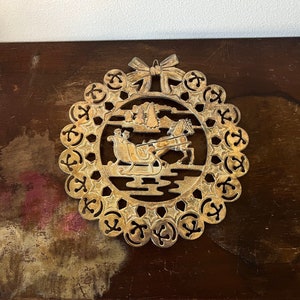 May include: A gold-colored metal Christmas ornament featuring a cut-out design of a horse-drawn sleigh with a bow at the top.