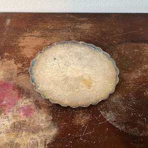 May include: A silver-plated tray with an ornate, scalloped edge and a detailed floral design. The tray is circular and has a slightly raised centre.