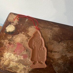 May include: A brown, Santa Claus-shaped ornament with a red string for hanging. The ornament features a detailed depiction of Santa holding a basket. The words "Father Christmas" are at the bottom.