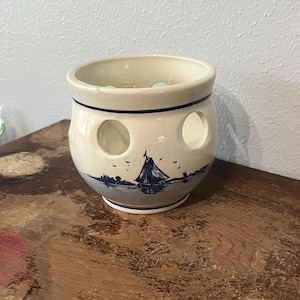 May include: Cream-colored ceramic bowl with a blue nautical scene featuring a sailboat. The bowl has three circular openings and a dark blue trim. The design includes a sailboat, birds, and a shoreline.