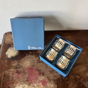 May include: Set of four silver napkin rings in a blue box with the William Adams logo. The rings have a decorative, openwork design.