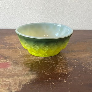May include: A small, green and yellow glass bowl with a textured, diamond-shaped pattern. The bowl is made of milk glass and has a white interior.
