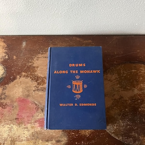 May include: A blue hardcover book titled "Drums Along the Mohawk" by Walter D. Edmonds. The book cover features an illustration of a drum with a red and orange design.