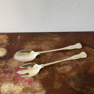 May include: A set of silver salad serving utensils, a spoon and a fork, on a wooden surface.