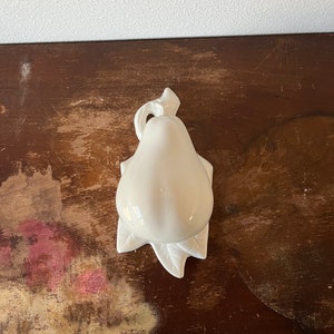 May include: White ceramic pear-shaped dish with a leaf design. The dish is sitting on a dark brown wooden surface.