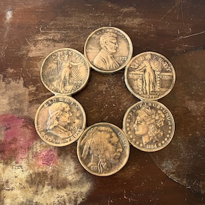 May include: A collection of six silver-colored US coins arranged in a circle on a brown wooden surface. The coins feature different presidents and historical figures, including Abraham Lincoln, George Washington, and Sacajawea. The coins are dated from 1913 to 1972.