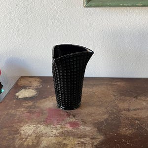 May include: A black glass vase with a geometric pattern. The vase has a curved shape and a wide opening.