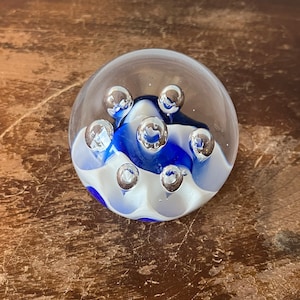May include: A glass paperweight with blue and white swirls and multiple air bubbles inside.