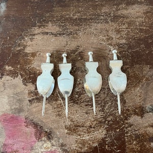May include: Four silver cocktail picks with decorative handles. The picks are arranged in a row on a wooden surface.