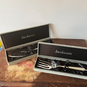 May include: Two silver serving pieces in their original boxes. The boxes are lined with gray velvet and have the name "Jacobson's" printed on the top. The serving pieces are a knife and a fork.
