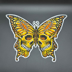 May include: A yellow and orange embroidered butterfly patch with a skull design. The butterfly wings are detailed with black stitching and the skull has white teeth.