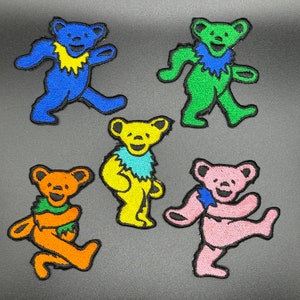 Peut inclure: Cinq patchs brodés colorés de ours dansants. Les ours sont bleus, verts, jaunes, oranges et roses. Chaque ours a un design unique et une expression joyeuse.