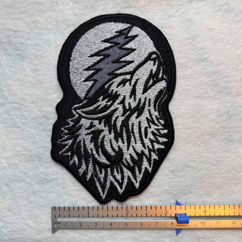 May include: Embroidered patch featuring a howling wolf silhouette against a full moon and a lightning bolt. The patch is outlined in black, with the wolf and moon in shades of gray. The patch measures approximately 4 inches in height.