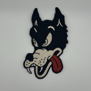 May include: An embroidered patch featuring a cartoon wolf with a red tongue sticking out. The wolf has a black and white design and a menacing expression, looking to the left.