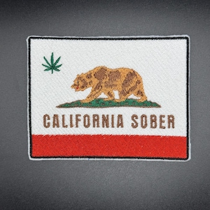Puede incluir: Parche bordado con el diseño de la bandera del estado de California, con un oso, una hoja de cannabis y la frase "CALIFORNIA SOBER". El parche tiene un fondo blanco, una franja roja y un borde negro.