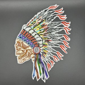 May include: Embroidered patch of a skull wearing a colorful Native American headdress. The skull is brown and the headdress is white, red, yellow, blue, and green.
