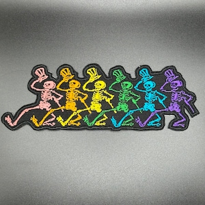 May include: Rainbow colored skeleton figures wearing top hats and dancing in a line. The figures are embroidered on a black patch.
