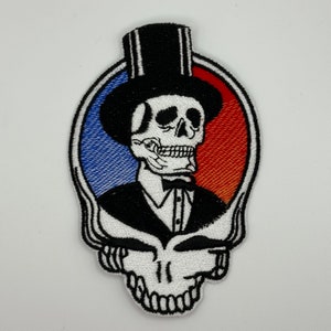 May include: White embroidered patch featuring a skull wearing a top hat and a tuxedo. The skull is set against a red, white and blue background.
